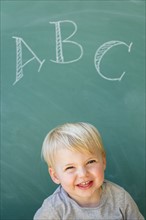 Boy (2-3) smiling in front of blackboard with letters ABC written on it