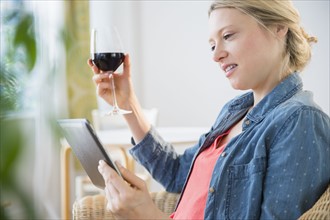Woman sitting with digital tablet and glass of red wine