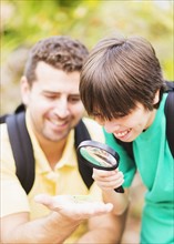 Father and son (12-13) watching insect with magnifying glass