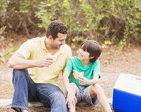 Father and son (12-13) eating sandwiches in forest