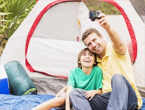 Father and son (12-13) taking selfie in front of tent