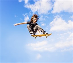 Man jumping on skateboard against sky and clouds