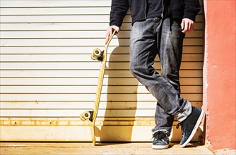 Man with skateboard leaning on garage door
