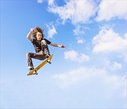Man jumping on skateboard against sky and clouds