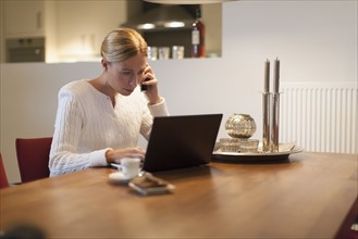 Woman using laptop and cell phone at home