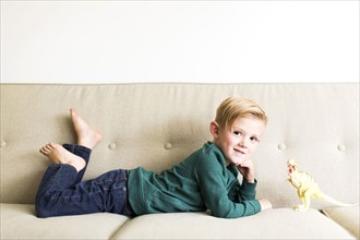 Boy (2-3) lying on sofa with toy dinosaur