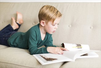 Boy (2-3) reading book on sofa