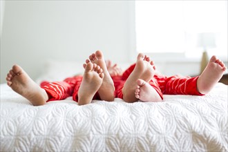 Siblings (2-3, 4-5) in red pajamas lying on bed