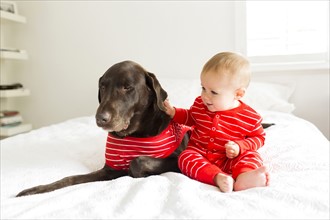 Boy (2-3) in red pajamas stroking dog