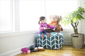 Girl (4-5) sitting with teddy bear on bean bag