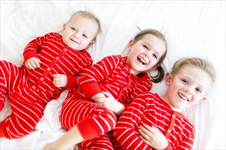 Girl (4-5) and two brothers (6-7) lying on bed in striped pajamas