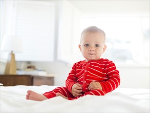 Boy (2-3) in striped pajamas sitting on bed