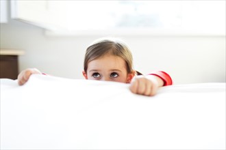 Girl (4-5) peeking over bed edge