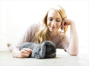 Young woman lying on floor and stroking rabbit