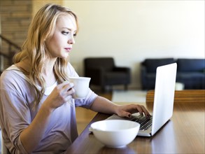 Young woman using laptop and drinking coffee at table