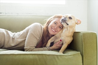 Woman lying on sofa embracing pug