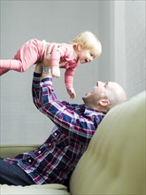Father sitting on sofa holding baby son (2-3) in air