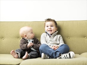 Baby boy (2-3) and brother (6-11 months) sitting on sofa