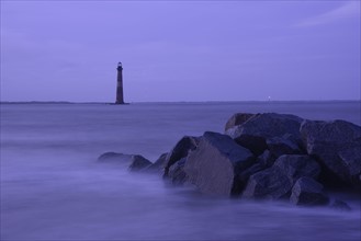 Coastal rocks and lighthouse silhouetted as dusk