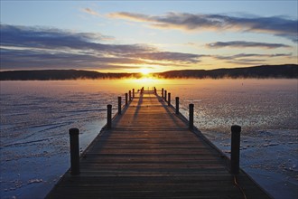 Symmetrical view of jetty on frozen lake, hills in background at sunrise