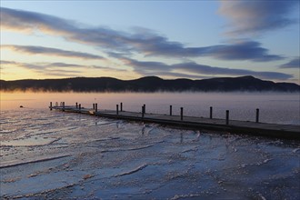 Jetty on frozen lake with vapor, hills in background at sunrise
