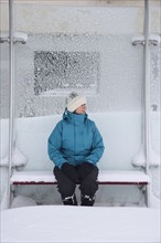 Middle aged woman sitting in bus stop, winter snow