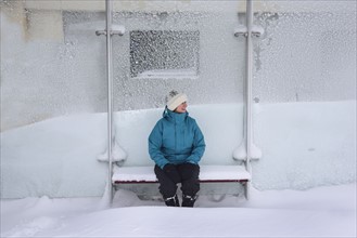 Middle aged woman sitting in bus stop, winter snow