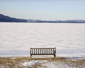 Park bench at edge of a frozen snowed lake, hills in background