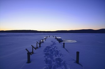 Symmetrical image of snowed jetty with footprints at dawn, hills on horizon
