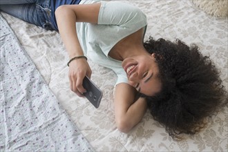 Teenage girl (16-17) texting in bedroom.