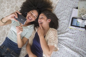 Teenage girls (14-15, 16-17) texting in bedroom.