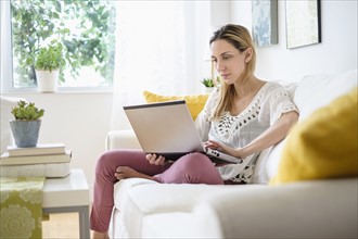 Woman with laptop sitting on sofa .