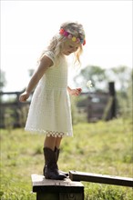 Cute girl (4-5) in white dress standing on fence in meadow