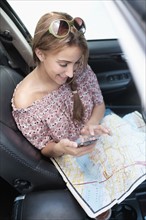 Woman checking phone in car with map on lap.