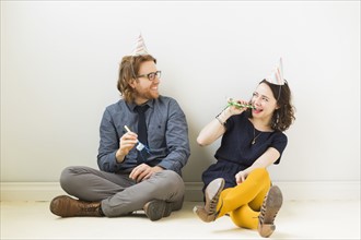 Couple with party horn blowers and party hats sitting on floor
