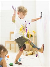 Boy (2-3) painting on wall with hands and legs