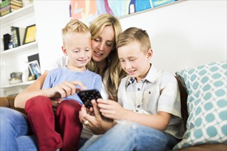 Mother with children (4-5, 6-7) using smartphone on sofa