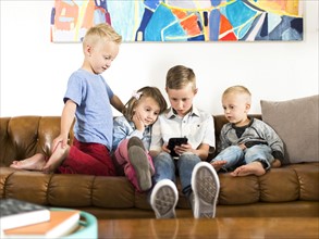 Children (2-3, 4-5, 6-7) sitting on sofa and using smartphone