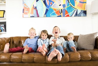 Smiling children (2-3, 4-5, 6-7) sitting on sofa
