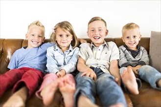 Smiling children (2-3, 4-5, 6-7) sitting on sofa