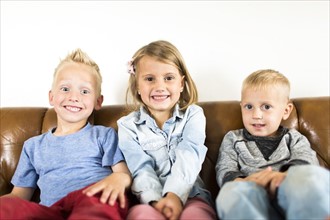 Smiling children (2-3, 4-5) sitting on sofa