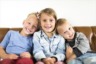 Smiling children (2-3, 4-5) sitting on sofa