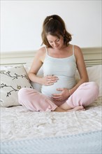 Smiling pregnant woman sitting on bed.