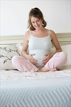 Smiling pregnant woman sitting on bed.