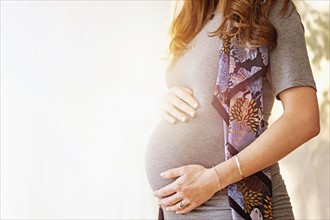 Mid-section of pregnant woman outdoors.