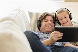 Man using tablet pc with his son (8-9) on sofa.