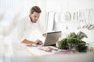 Chef using laptop in kitchen.