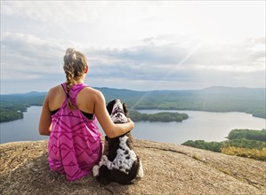 Young woman sitting with dog on cliff looking at lake view