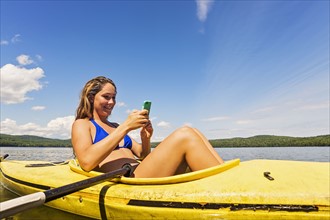Young woman using Smartphone in kayak on lake