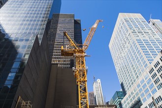 Low angle view of crane among skyscrapers